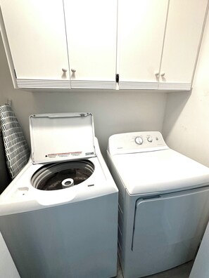 A laundry area with two washing machines and a dryer, a ventilation unit, and white cabinets above. - Home in Panama City - Seahorse Oasis (Panama City)