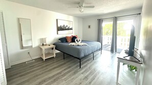 A bedroom with a bed, a nightstand, a ceiling fan, a window with curtains, and a television on a stand. - Home in Panama City - Seahorse Oasis (Panama City)