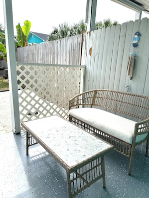 A wicker sofa with a cushion, a matching table, and a wooden fence in the background. - Home in Panama City - Seahorse Oasis (Panama City)