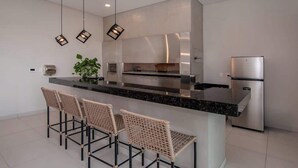 A modern kitchen with a central island, stainless steel appliances, and three wicker bar stools. - Corporate Stays CorAr 1L (Asunción)