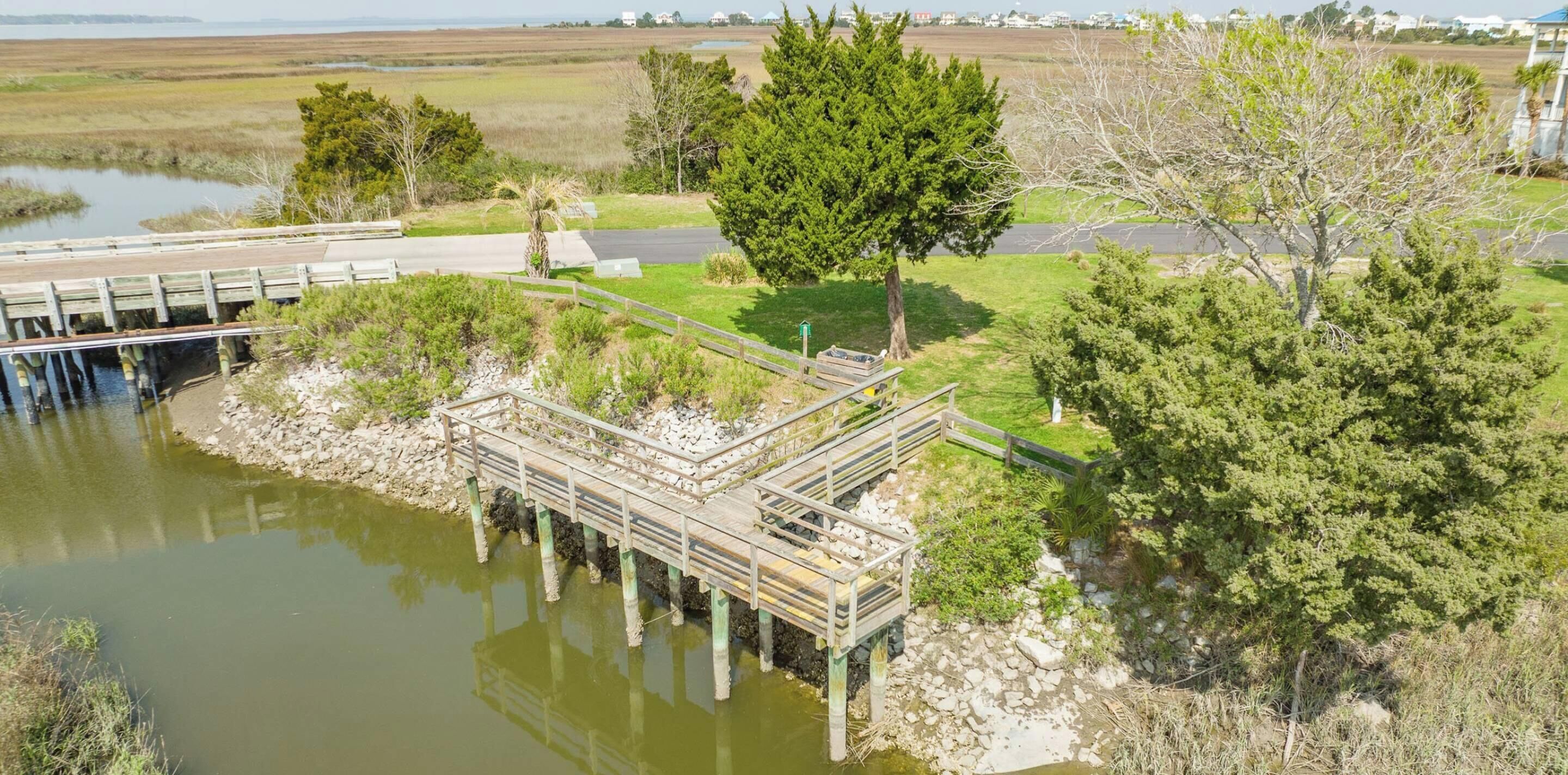 A wooden bridge over a body of water, surrounded by greenery and a clear sky.