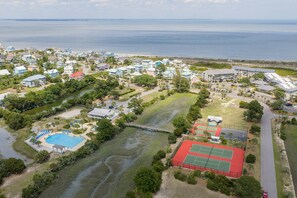 An aerial view of a coastal residential area with houses, a tennis court, and a swimming pool.