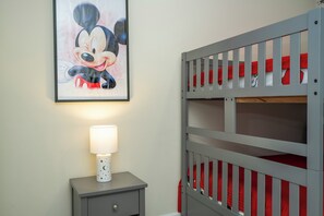 A child's bunk bed with red bedding, a nightstand with a lamp, and a framed picture of a cartoon character on the wall. - 3BR Condo at Champions Gate Resort near Disney (Kissimmee)