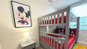 Ein Kinderzimmer mit Etagenbetten, einem gerahmten Comicfiguren-Bild, einem Nachttisch und einem Fenster mit Sternenmustern.