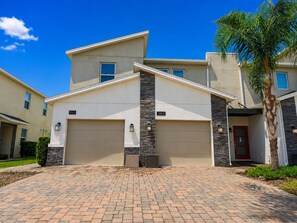A modern two-story house with a garage, a stone accent wall, and a red door. - 3BR Condo at Champions Gate Resort near Disney (Kissimmee)