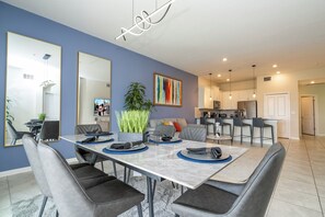 A modern dining area with a marble table, grey upholstered chairs, and a large mirror on the wall. - 3BR Condo at Champions Gate Resort near Disney (Kissimmee)