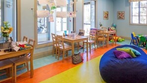 Ein Zimmer mit großem Fenster, einem Tisch mit Stühlen, einem Sitzsack und einem farbenfrohen Boden.
