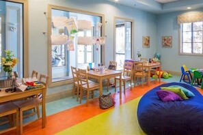 Ein Zimmer mit großem Fenster, einem Tisch mit Stühlen, einem Sitzsack und einem farbenfrohen Boden.
