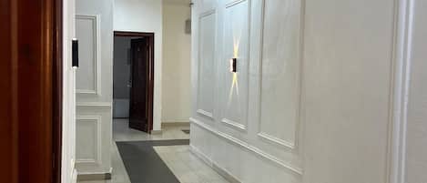 Un pasillo con paredes blancas, alfombra negra y un marco de puerta de madera.