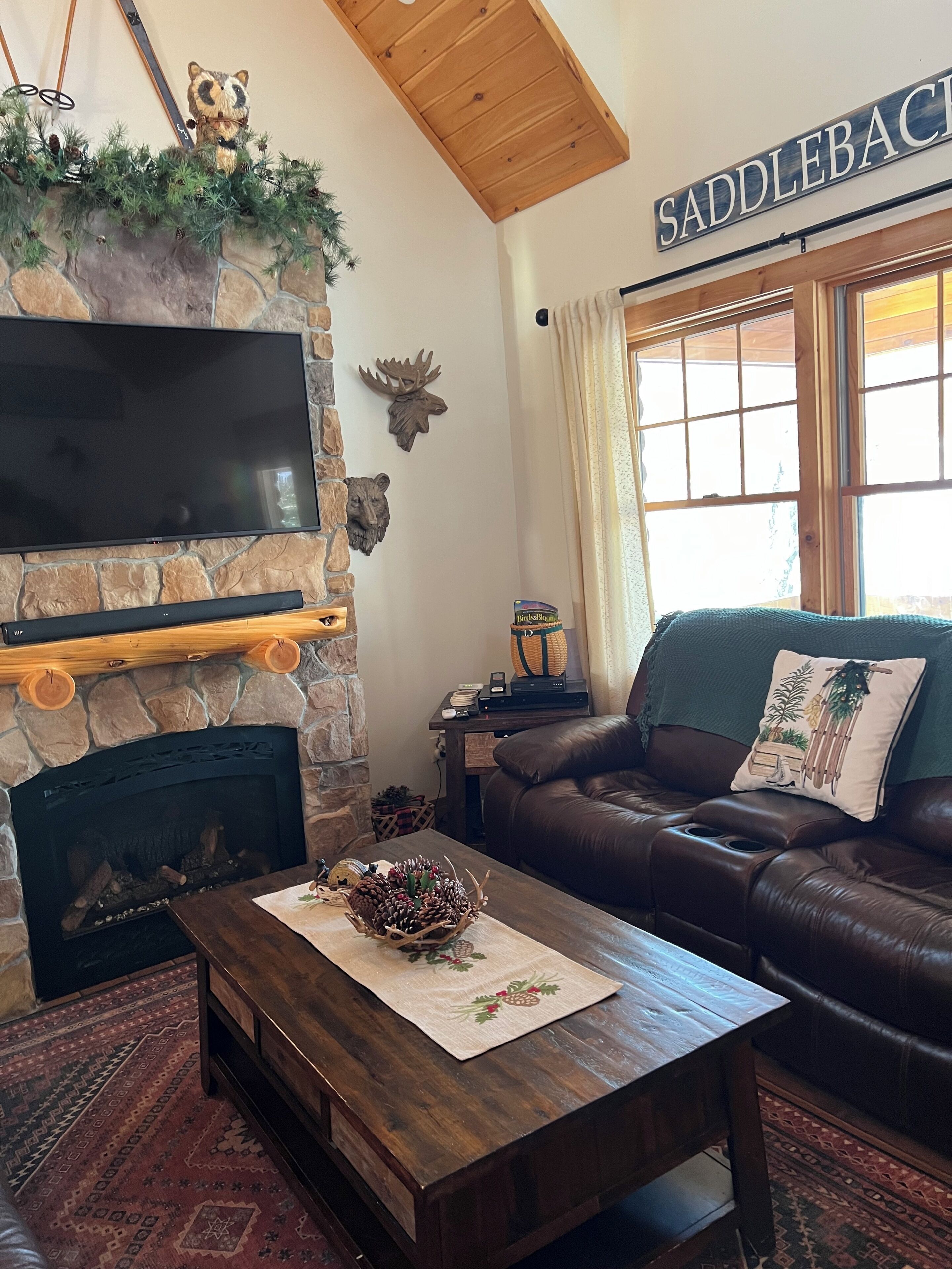 A cozy living room with a stone fireplace, a leather sofa, a flat-screen TV, and a sign reading 'SADDLEBACK.'
