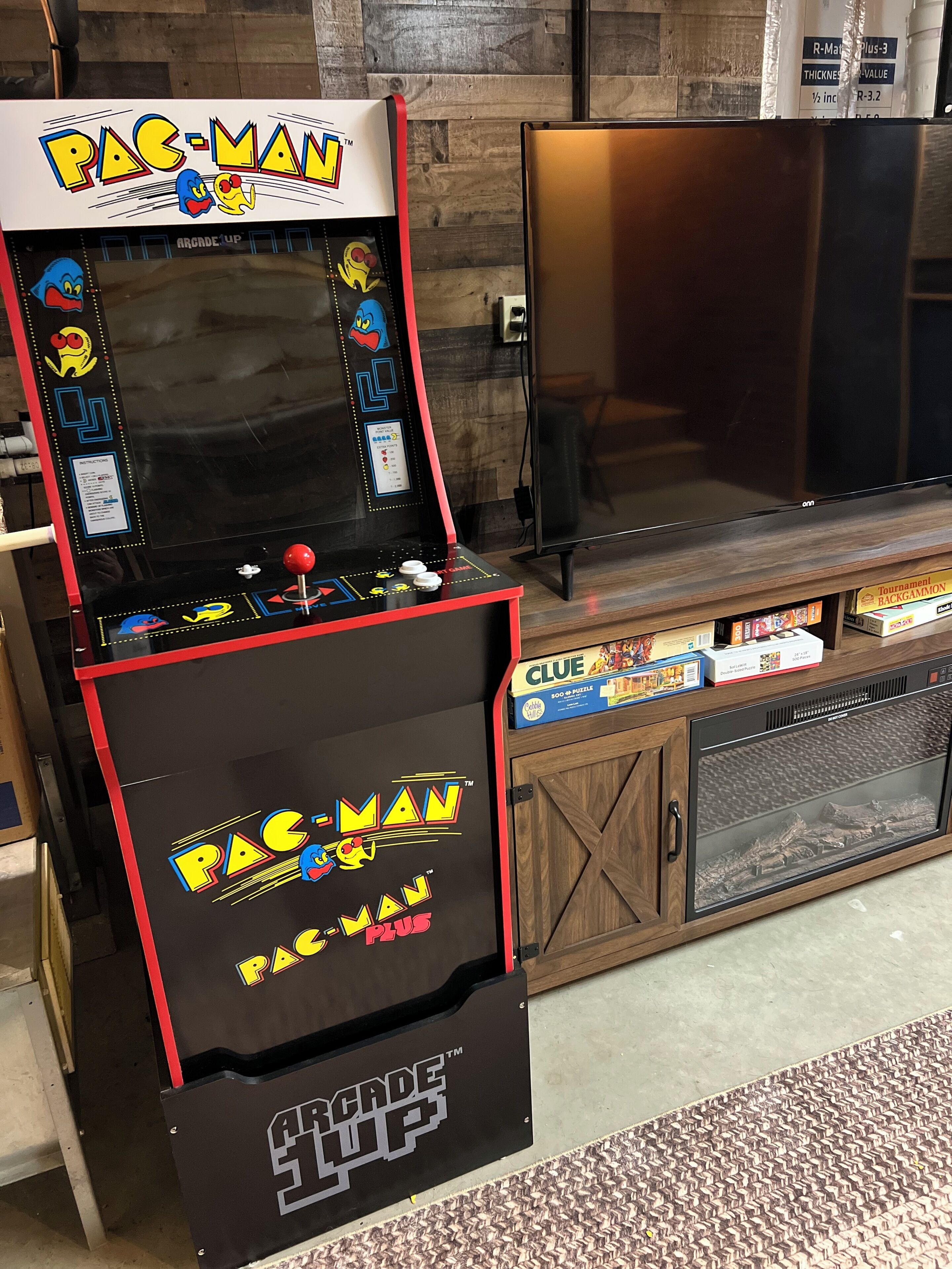 A Pac-Man arcade machine with a cabinet, a television, and a cabinet with board games.