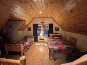 A cozy attic bedroom with wooden beams, two beds with patterned bedding, a desk, and a window with curtains. - Rangeley Cabin Close to Saddleback, Trails, and Lake. Sleeps 8- Pet friendly (Dallas Plantation)