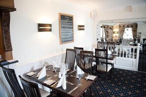 A dining area with a table set for four, a chalkboard menu, and a patterned carpet.