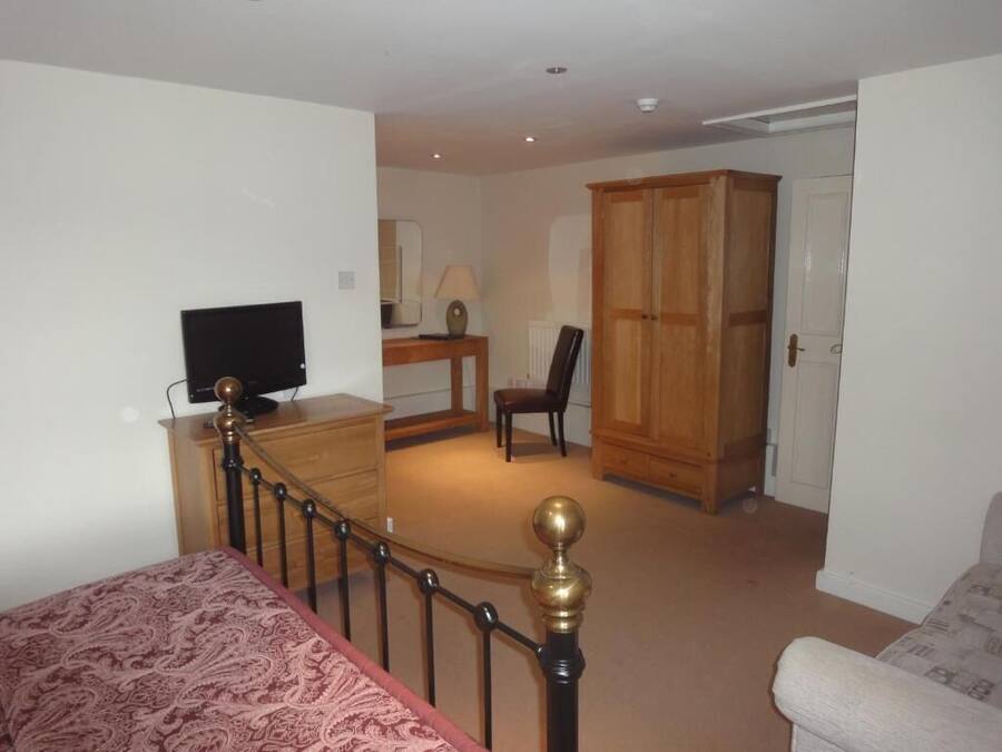 A bedroom with a bed, a television, a wooden wardrobe, and a desk with a chair.