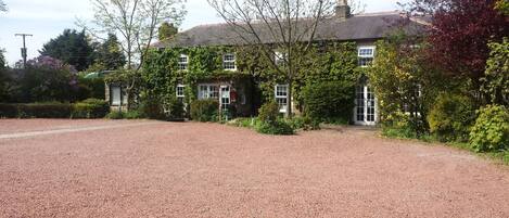 A building with a gravel driveway, surrounded by greenery and trees.