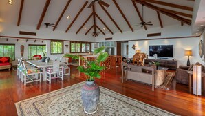 A spacious living area with wooden beams, a dining table, chairs, a sofa, a TV, and a large vase with plants. - Residence Disa – Panoramic sea views above Patong Bay, just steps from the beach (ตำบลป่าตอง)