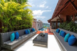 Eine Dachterrasse mit einer langen Bank, einem Couchtisch und Blick auf das Meer.