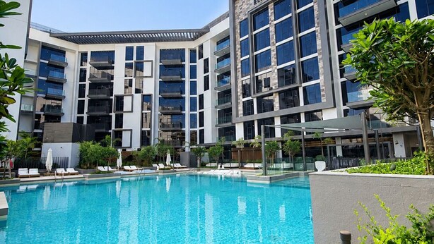 Un hôtel moderne doté d’une piscine, de nombreux balcons et offrant une vue sur un ciel d’un bleu éclatant.