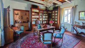Une pièce avec un plafond en bois, un lustre, une grande bibliothèque, une table avec des chaises et un tapis à motifs.