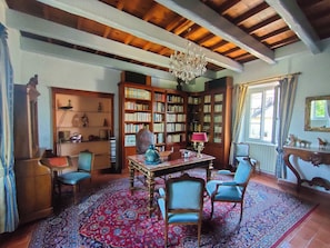 Une pièce avec un plafond en bois, un lustre, une grande bibliothèque, une table avec des chaises et un tapis à motifs.