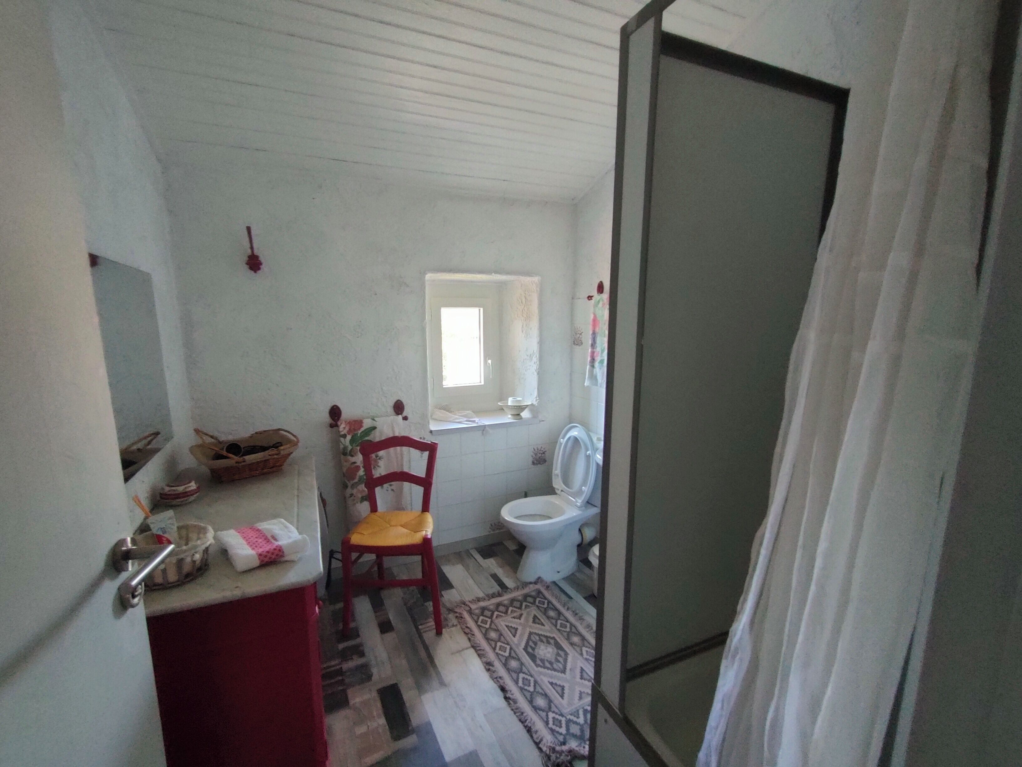 Un baño con inodoro, ventana, silla y lavamanos.