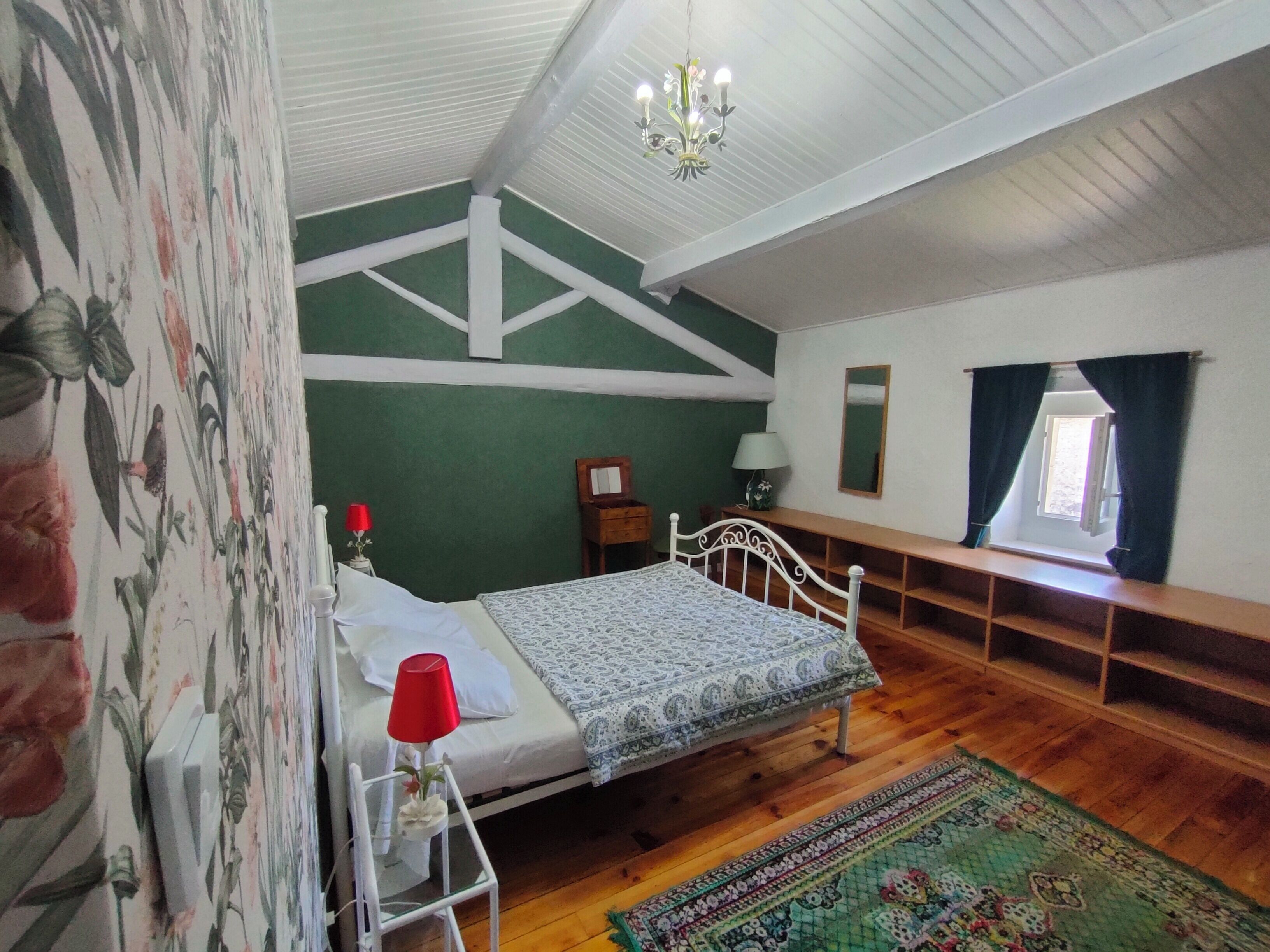 Un dormitorio con cama, mesita de noche, cómoda, espejo, ventana con cortinas y candelabro.