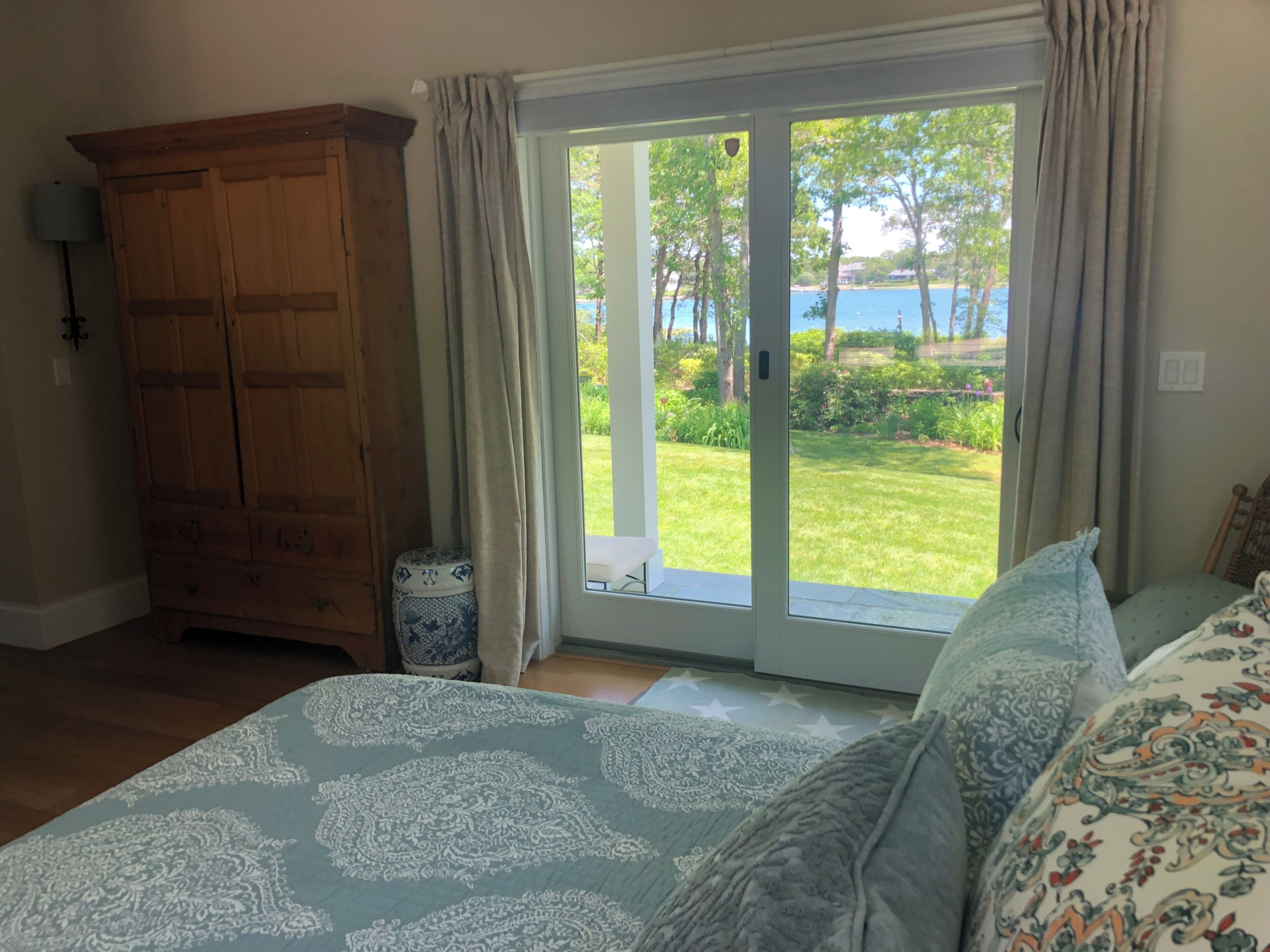 Une chambre à coucher avec un grand lit, une armoire en bois et une porte-fenêtre coulissante donnant sur un jardin.
