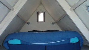 Une petite pièce mansardée fermée, avec un lit simple, une fenêtre et des murs inclinés.