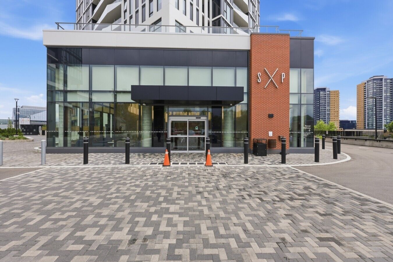 Um edifício moderno com fachada de vidro, um logotipo 'SXP' bem visível e um pavimento estampado na frente.
