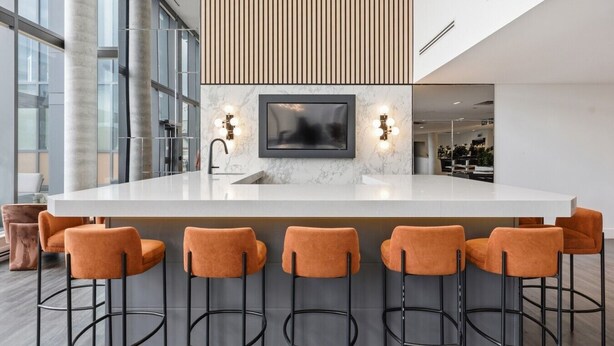 A modern kitchen with a marble countertop, a built-in TV, and bar stools.
