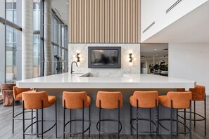 A modern kitchen with a marble countertop, a built-in TV, and bar stools. - Stylish 2BR in Station Park | Private Patio + Spa, Gym & Bowling (Kitchener)