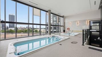 Piscina interior moderna com vista ampla para a paisagem urbana através de grandes janelas.