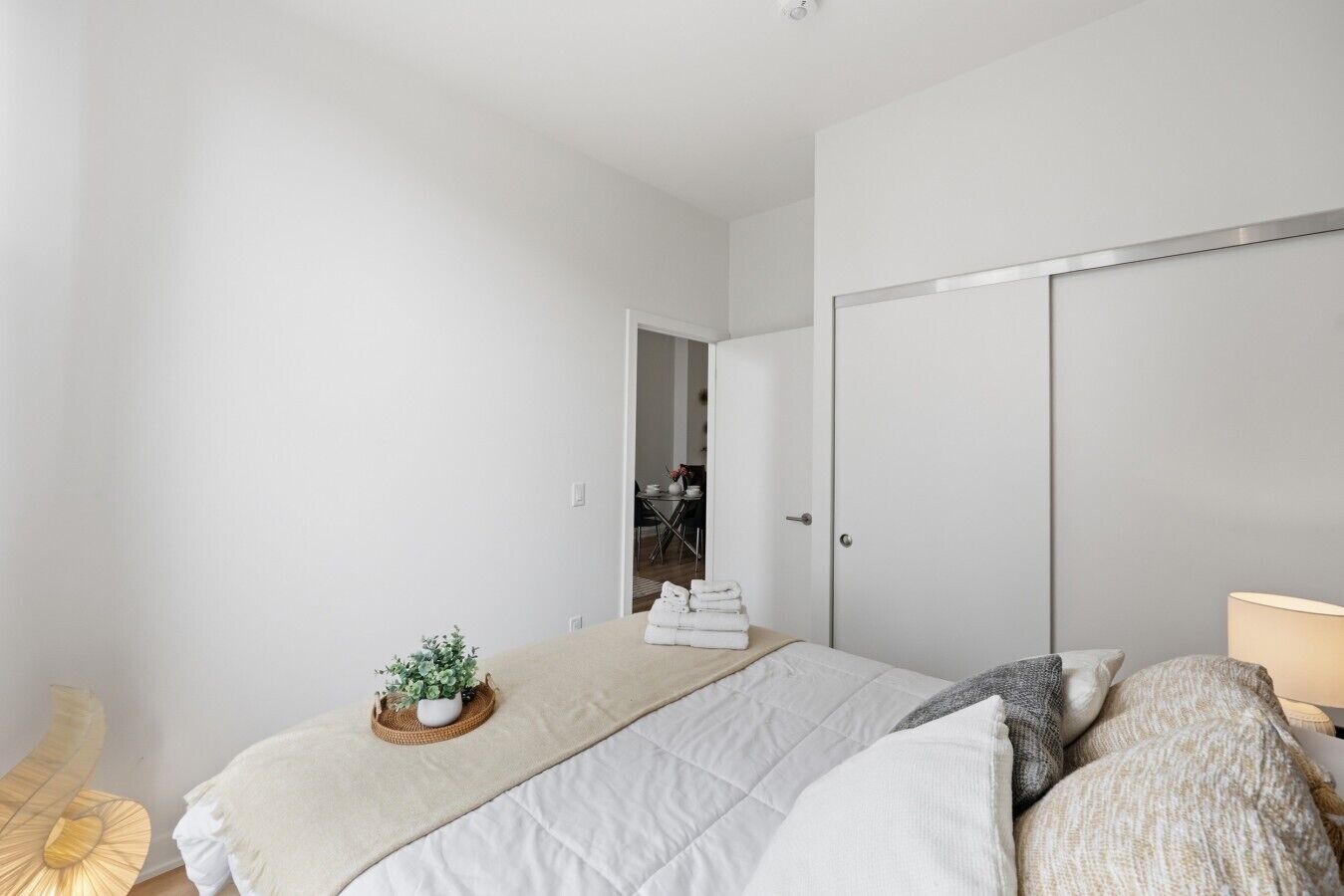 Un dormitorio con cama, mesita de noche, lámpara, planta en maceta y armario.
