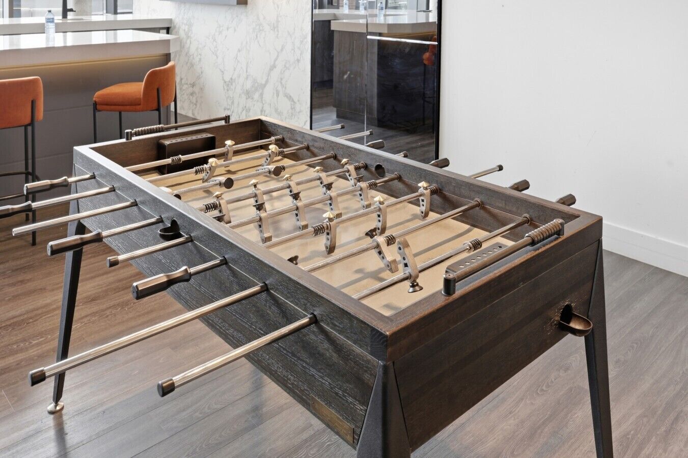 Een tafelvoetbaltafel in een moderne keuken met marmeren aanrechtbladen en een houten vloer.