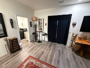 Un salon avec un rideau foncé, une table ronde, un petit tabouret, une lampe décorative et un tapis à motifs.