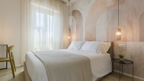 Een slaapkamer met een bed, een stoel, een klein tafeltje en een wandlamp.