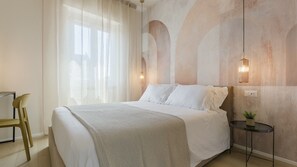 A bedroom with a bed, a chair, a small table, and a wall-mounted lamp. - Tabata Home (Milano)