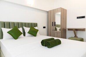 Ein modernes Hotelzimmer mit einem Bett, grünen Kissen, einem Holzschrank, einem Spiegel und einem kleinen Schreibtisch.