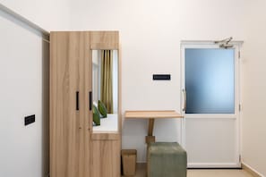 Ein Zimmer mit Holzschrank, kleinem Tisch, Bank, Tür mit Milchglas und Lichtschalter an der Wand.