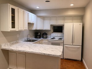 Una cocina con armarios blancos, encimera de mármol, estufa, refrigerador y cafetera.