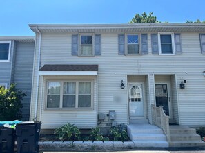 A two-story house with a front porch, a door with a glass panel, and a small set of steps leading to the entrance.