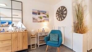 Una habitación con un armario de madera, un sillón azul, un reloj de pared y varias fotografías enmarcadas.