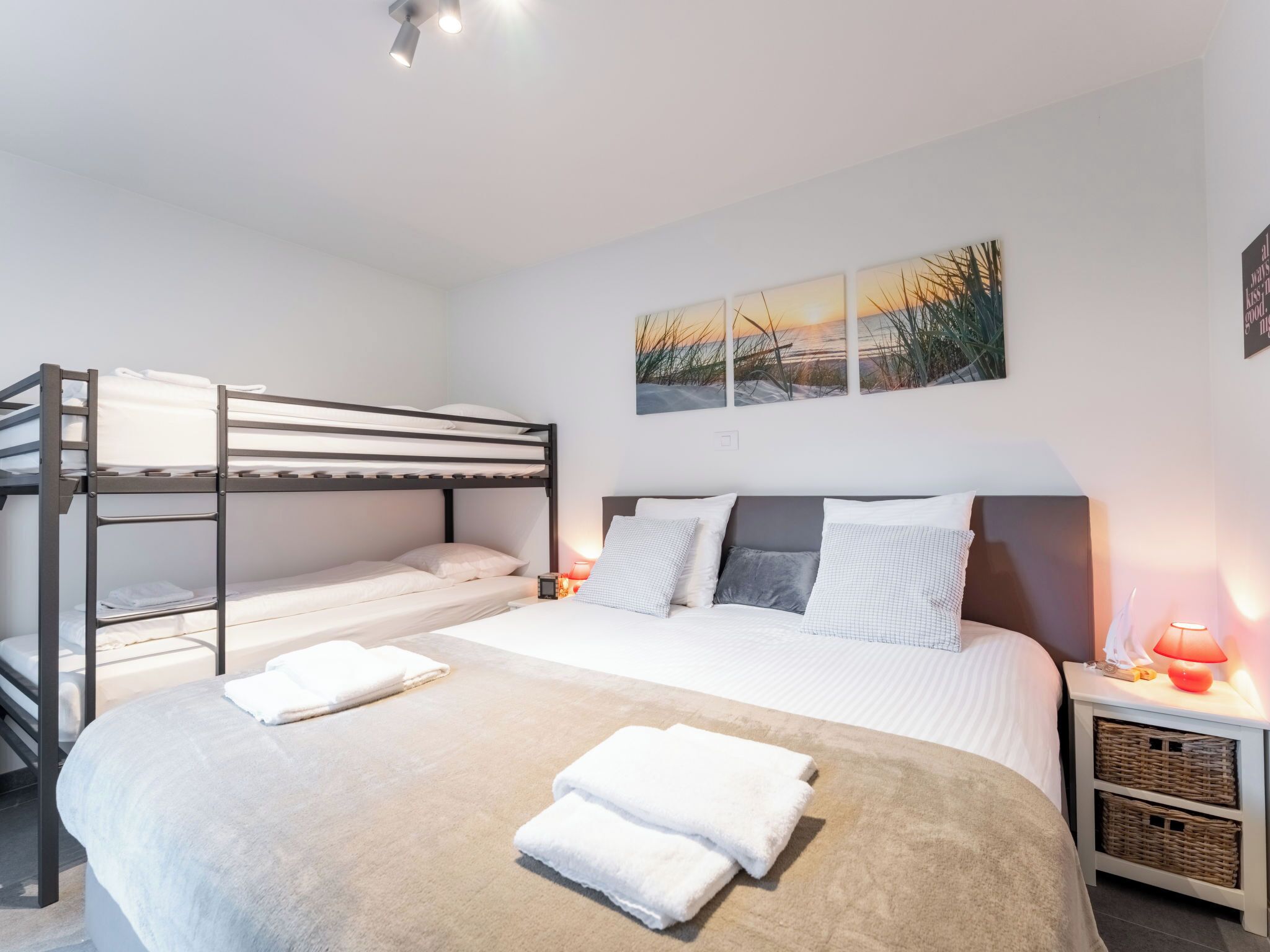 A bunk bed room with a large bed, a nightstand with a lamp, and a painting on the wall.