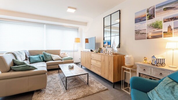 Una sala de estar moderna con un sofá, una mesa de centro y un aparador. Se ve una ventana con persianas, una lámpara y un espejo fijado a la pared.