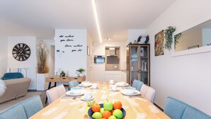 Un comedor moderno con una mesa de madera dispuesta para cuatro, un frutero en el centro y una cocina al fondo.