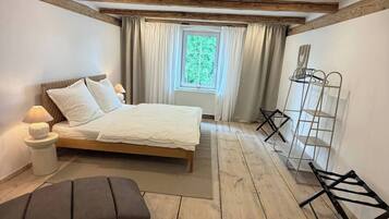 Ein Schlafzimmer mit Holzboden, einem Bett, einer Bank, einem Fenster mit Vorhängen und einem Metallregal.