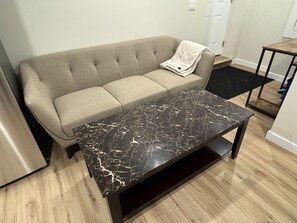 A beige sofa with a marble coffee table in a room with wooden flooring and a small table with a black table runner. - Newly Finished Lookout Secondary Suite (Calgary)