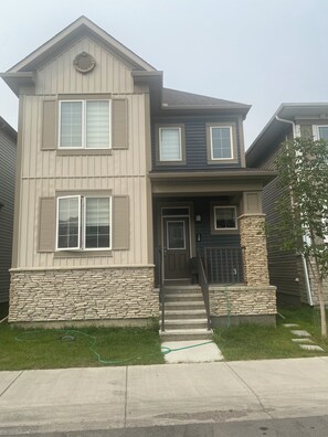 A two-story house with a stone foundation, a front door, and a garage. - Newly Finished Lookout Secondary Suite (Calgary)