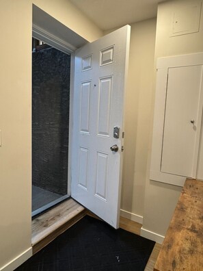 A white door with a metal handle, a black mat at the entrance, and a wooden bench to the right. - Newly Finished Lookout Secondary Suite (Calgary)