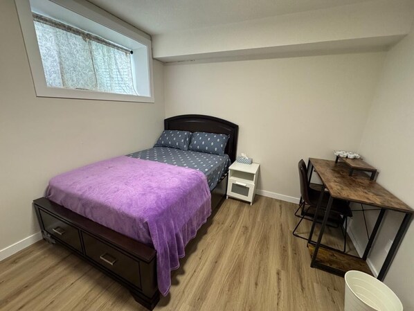 Een slaapkamer met een bed, een klein bureau, een stoel, een raam en een nachtkastje.